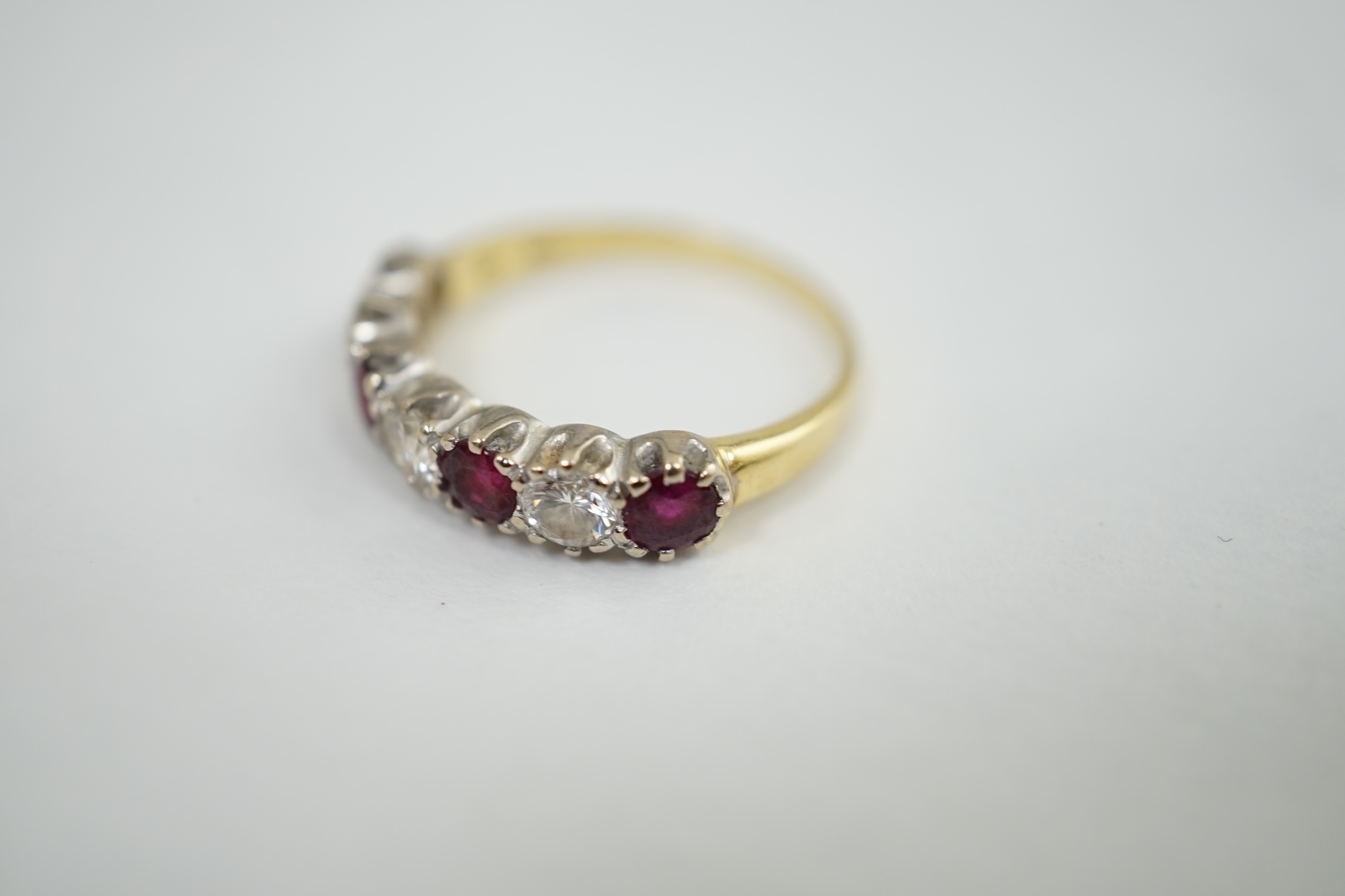 An 18ct yellow and white gold three stone diamond and four stone ruby set half hoop ring